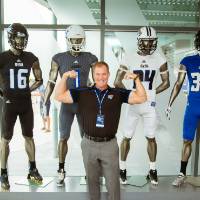 A guest flexing his biceps, posing in front four mannequins wearing jerseys at the Jamie Hosford Football Center dedication.